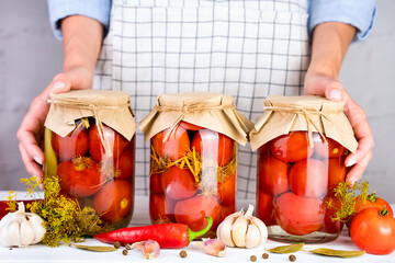 Woman's hands hold jars of homemade organic pickled tomatoes with garlic, dill, and spices. Traditional homemade preparations for the winter. Close-up.