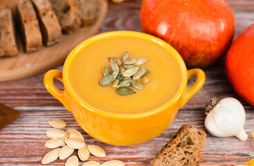 Delicious pumpkin cream soup and and crispy rye bread on a wooden table. Homemade food made from seasonal vegetables. Close-up. Selective focus.