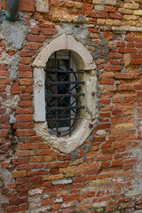 A small arched window rests hidden in the brick wall of Venice, Italy. Worn stones and rusty bars tell stories of age and strength. The wall carries both charm and silence of forgotten times.