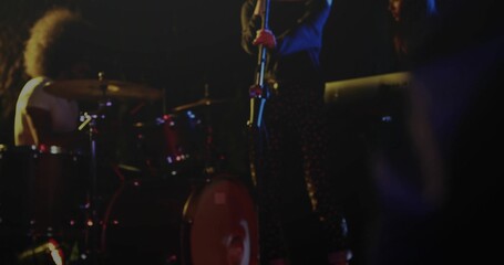 Singer in patterned pants performing on stage holding mic stand, with red drum kit and lights