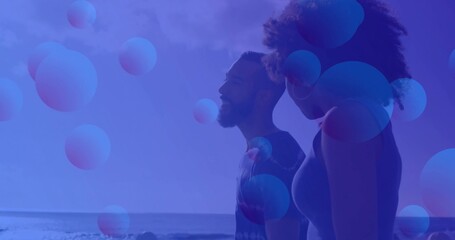 Standing couple wearing tank top, t-shirt on shore with ocean horizon floating spheres, copy space