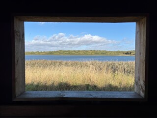 View through a wildlife hide window overlooking a lake and reed bed