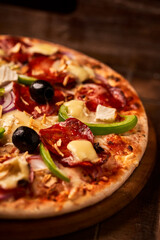 Pizza with chorizo ​​sausage, mozzarella cheese, green pepper and black olives. Rustic wooden background. Soft focus.	