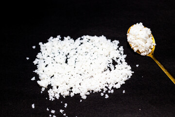 Pile of sea salt crystals and golden spoon against a black surface, showcasing culinary ingredients and a minimalist aesthetic suitable for food photography and healthy lifestyle themes