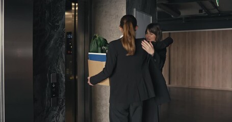 Girl in business clothes sees off her colleague who is walking with a moving box and entering the elevator leaving the office. Exceeding colleagues after being fired