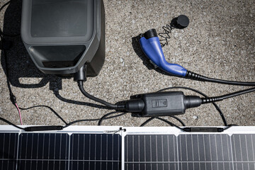 DYI implementation of using portable power station and flexible solar panels to charge electric vehicle. Cables and equipment placed on concrete surface of a driveway to collect free electricity.