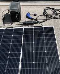 Detailed image of a solar power system with panels linked to a portable battery generator and ev charging cable. The setup includes charging cables and connectors on a concrete surface.