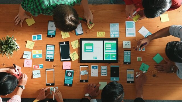Top view of developer team working together to write idea about Ux ui design on colorful sticky note. Group of programmer looking at wireframe prototype at tablet and designing software. Convocation.
