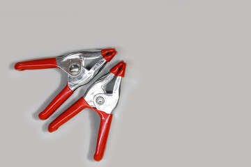 Two heavy duty house hold metal clamps with red handles on grey background.
