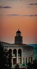 A peaceful moment as the sunrise, casting a warm, golden and orange light across the sky. In the foreground, a building with a unique, domed structure resembling a lighthouse stands proudly.