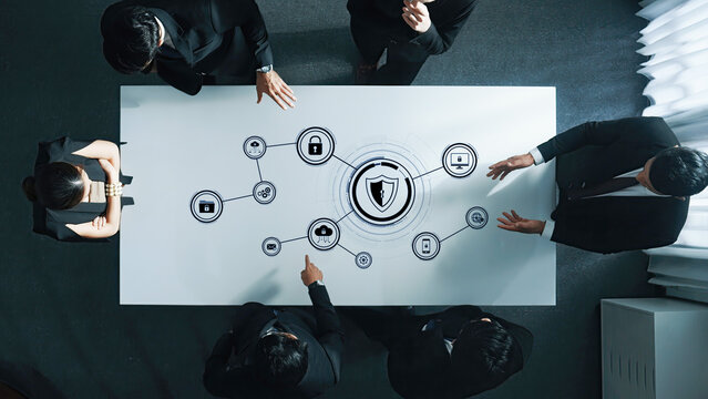 A group of business professionals engage in a discussion on cybersecurity strategies, surrounded by digital icons representing security measures and data protection. Trope