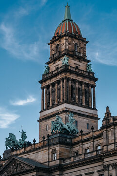 Close-up of the historic Wayne County Building in Detroit, Michigan, showcasing its ornate Beaux-Arts architecture, dome tower, and bronze quadriga statues against a blue sky.