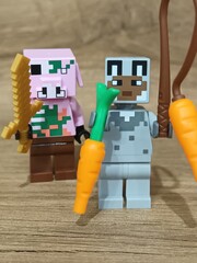 Obraz premium Whimsical block figures a pink pig-like character with a golden weapon and a grey animal holding a fresh carrot, posed on wood, symbolizing fantasy play and imaginative adventure