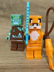 Naklejka premium Whimsical block figures a pink pig-like character with a golden weapon and a grey animal holding a fresh carrot, posed on wood, symbolizing fantasy play and imaginative adventure