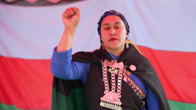 Proud mapuche woman in traditional clothing raising her fist in protest against the mapuche flag