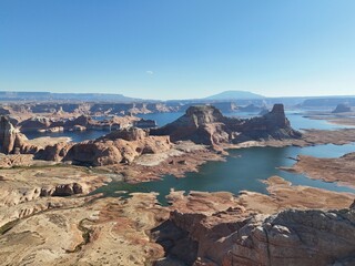 Aerial view of desert canyon with deep blue lake, layered rock formations, and distant mountains under clear sky