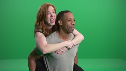 Woman with red hair on man's back, both smiling against green screen