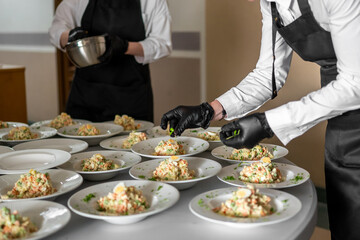 Professional chefs in black aprons and gloves plating multiple servings of Russian salad at a catering event, showcasing precise food presentation and teamwork.
