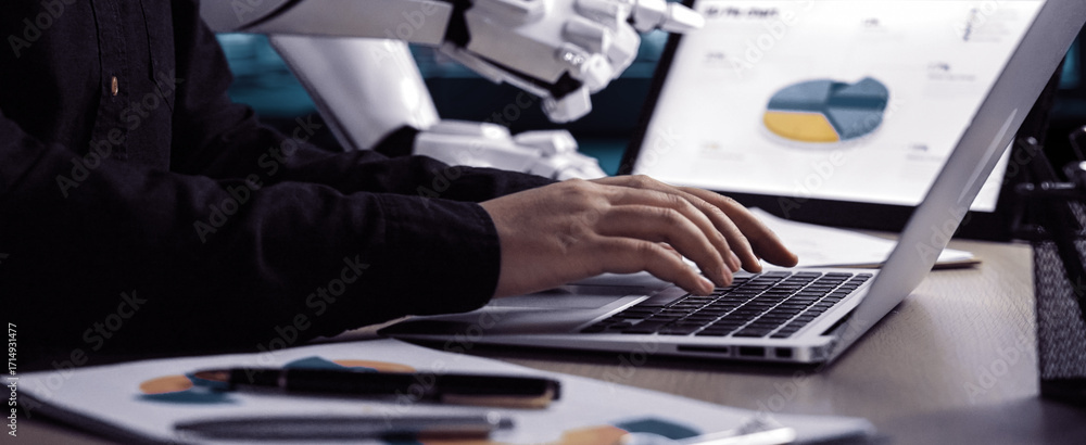 Poster A modern workspace showcasing a human interacting with a laptop while a robot assistant displays data analytics, emphasizing the fusion of technology and business processes.Noogenesis