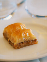 Baklava, 2 pieces, on a white plate on a set table, close-up, with a softly blurred background, side view