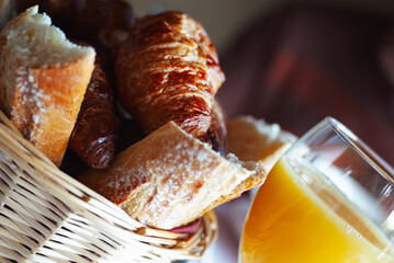 Close-up of a breakfast spread featuring flaky croissants, powdered sugar dusted bread slices, and a glass of vibrant orange juice, highlighting a hearty morning meal