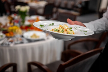 Close-up of person holding plate with gourmet salad at formal indoor banquet. Elegant table setting in background. Event catering, hospitality, and fine dining concept.