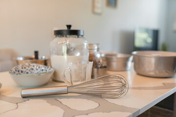 Baking tools and ingredients on kitchen counter with whisk in focus