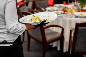 Waiter serving plated gourmet meals at formal event. Elegant table setup with white linens, banquet atmosphere, professional hospitality service