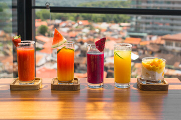 Colorful assortment of fruit juices on a wooden table with a city view.