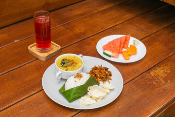Overhead shot of a meal with rice, curry, crackers, fruit, and a drink on a wooden table.
