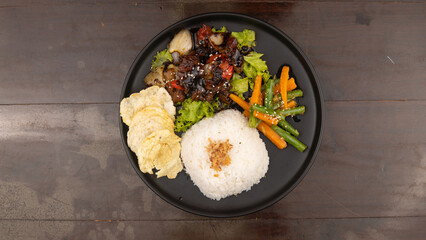 Overhead shot of a plate with rice, vegetables, crackers, and a dark sauce dish.