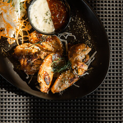 Delicious chicken wings with dipping sauce and coleslaw on a black plate.