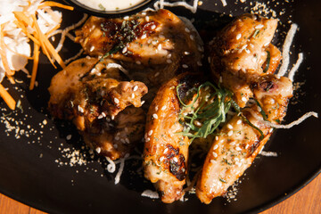 Close-up of grilled chicken wings with sesame seeds and garnish on a black plate.