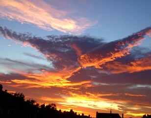 Fiery sunset clouds in molten bronze and indigo over silhouetted rooftops twilight