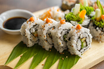 Sushi rolls on a wooden board with soy sauce and garnish.
