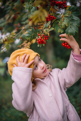 Child playing with red berries under a tree on a cool autumn day in a garden