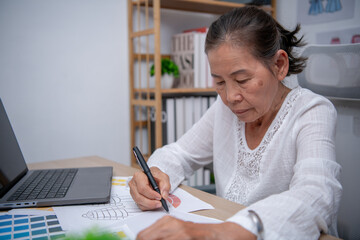 An elderly woman enjoys drawing and creating art in a cozy home workspace.