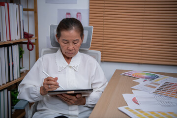 An elderly woman using a digital tablet to create designs in a modern workspace.