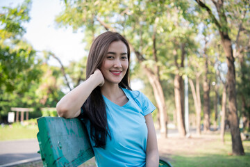 Smiling woman sitting on a park bench surrounded by lush greenery, enjoying nature.