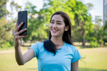 Smiling woman taking a selfie outdoors in a sunny park surrounded by greenery.