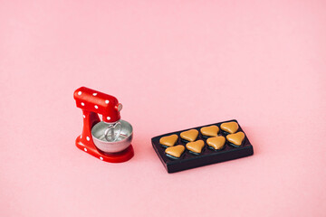 Mini stand mixer model with heart shaped cookies on pastel pink background. Minimal creative kitchen mixer with biscuits concept. Trendy sweet food idea.