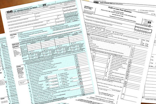 Tax year 2025 IRS 1040 and schedule c, profit or loss from business, forms lay on a desktop.