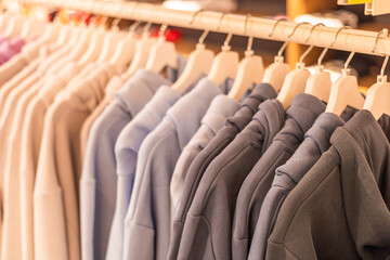 Obraz premium Hoodies displayed on hangers in a retail store. Various colors include gray, blue, and beige. The setting is bright and inviting, showcasing casual fashion.