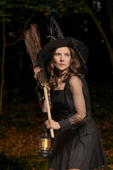Halloween witch with broom and lantern in dark forest closeup portrait