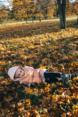 Little girl enjoying autumn in a park lying on fall foliage on a sunny day