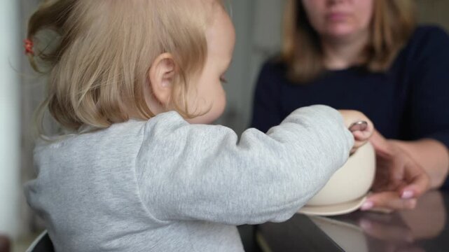 Blonde toddler is spoon-fed meal by nurturing adult, showcasing tender moment of parental care and early childhood