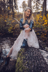 A young woman sitting on a fallen log by a stream in a forest wearing a tulle skirt and boots