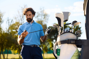 Naklejka premium Smiling golfer picking golf club out of his bag on course.