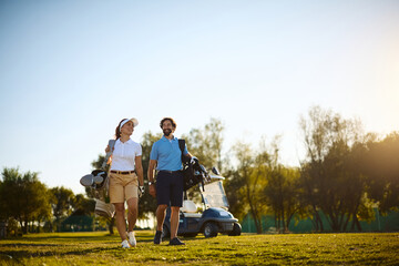 Obraz premium Happy couple with golf bags walking across course.