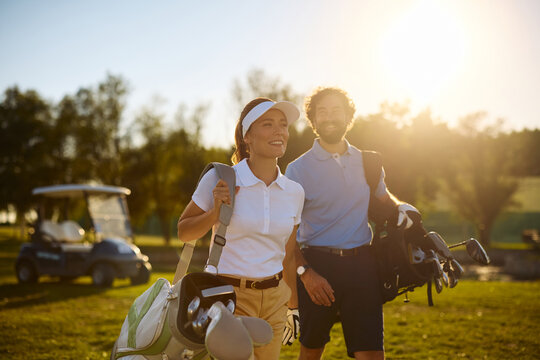 Happy couple of golfers enjoying in playing golf at sunset.